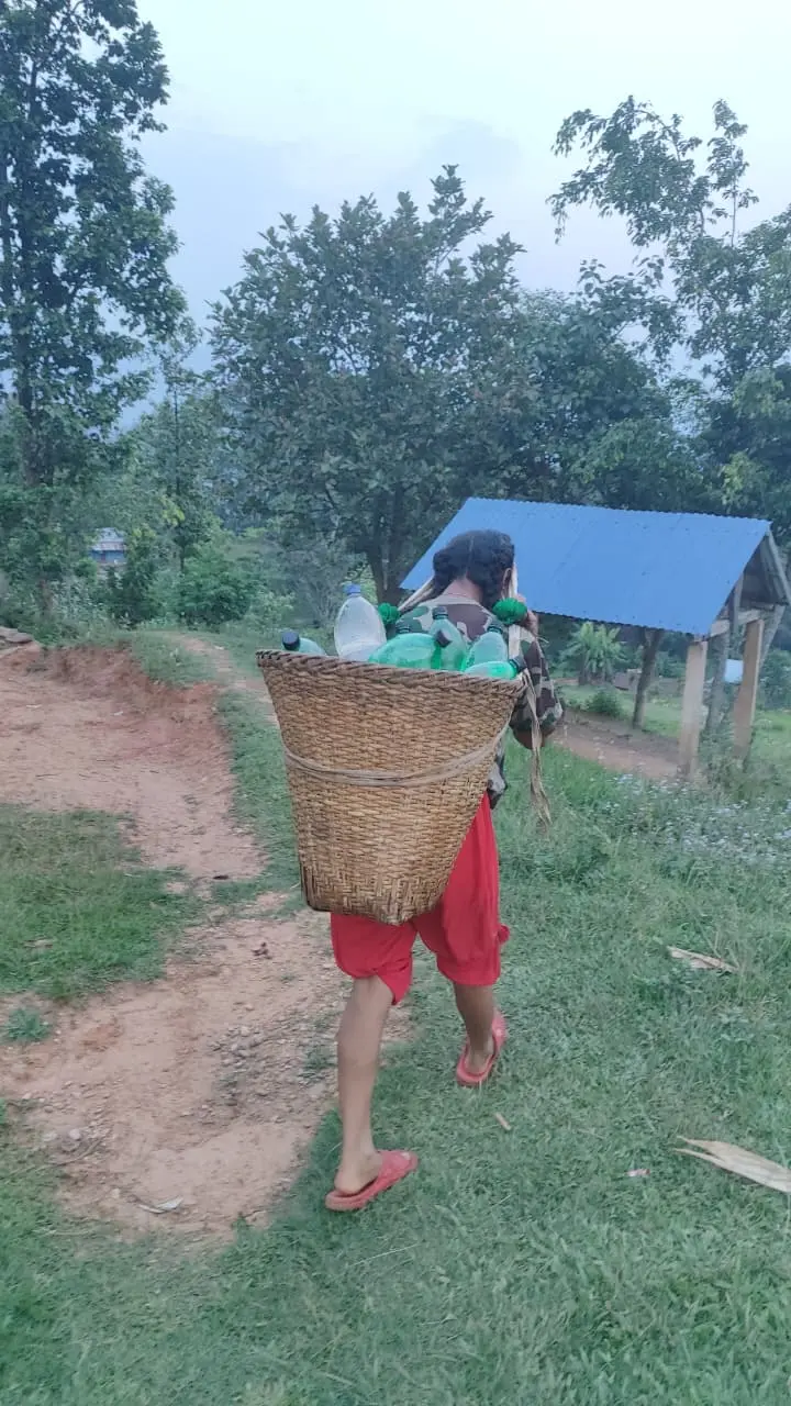 Een kind loopt door een landelijke omgeving in Nepal met een draagmand op de rug.